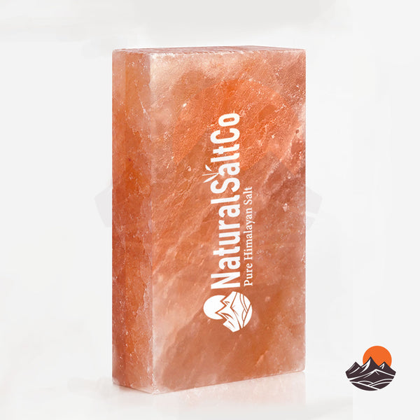 A rectangular block of Natural Salt Co. Himalayan salt, showing its characteristic orange-pink crystalline texture, with white branding printed vertically on the front face, set against a clean white background.