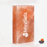 A rectangular block of Natural Salt Co. Himalayan salt, showing its characteristic orange-pink crystalline texture, with white branding printed vertically on the front face, set against a clean white background.