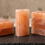 Three rectangular pink salt stone blocks arranged on a dark tabletop, with two stacked on each side and a blurred neutral background.
