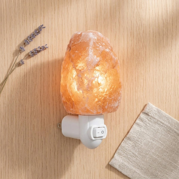Himalayan salt lamp on a wooden surface with lavender and a blanket.