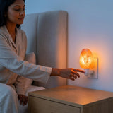 Woman in bed interacting with a night light on a bedside table.